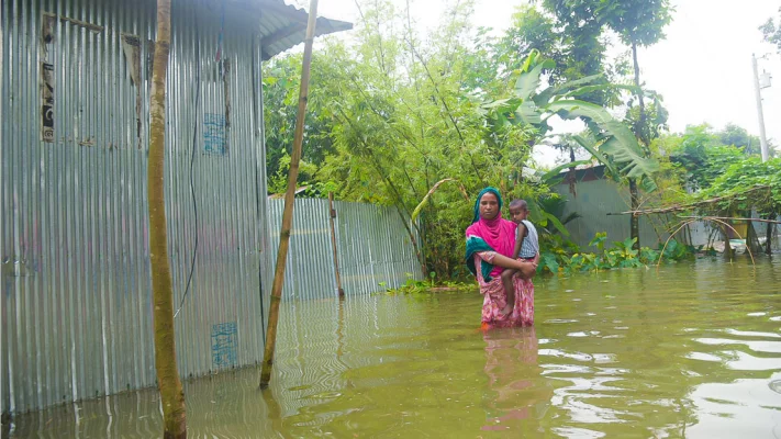 বাড়ি-ঘরে পানি ঢুকে পাড়ায় বাচ্চাকে কোলে করে নিয়ে হাঁটুপানিতে দাঁড়িয়ে আছেন এক নারী। লক্ষীটারী ইউনিয়নের চর বাগেরহাট এলাকা থেকে তোলা